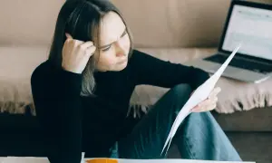Zmartwiona kobieta analizuje dokumenty, zastanawiając się, jak długo widnieje się w BIK po spłacie zadłużenia.