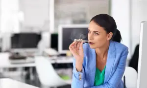 Kobieta w biurze zaciąga się e-papierosem, ignorując widoczny wszędzie zakaz palenia.