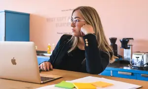 Kobieta w okularach zastanawia się, jak zatrudnić stażystę, siedząc przy laptopie.