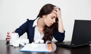 Zmęczona kobieta z kubkiem i chusteczkami przy laptopie. Zastanawia się, czy fizjo może wystawić L4.