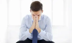 Zmartwiony mężczyzna w garniturze, z rękami złożonymi na czole, zastanawia się, czy niezdanie egzaminu zawodowego to nie zdam klasy.
