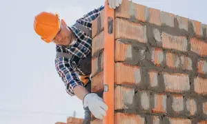 Murarz w kasku sprawdza pion muru libellą. Dbałość o detale to klucz do tego, jak pozyskać zlecenia budowlane.