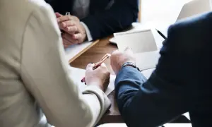 Ludzie przy stole omawiają dokumenty. Jeden z nich, jako zarządca sukcesyjny, wskazuje na notatki w notesie.