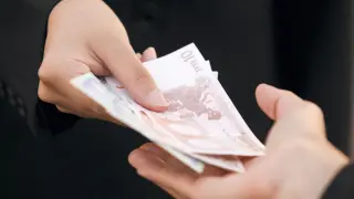Dwie dłonie przekazują sobie banknoty euro. Zastanawiasz się, ile kosztuje windykacja należności?