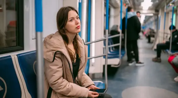 Młoda kobieta w beżowej kurtce siedzi w metrze, zamyślona. Może właśnie wraca z wizyty u lekarza, który wystawił jej zwolnienie lekarskie z powodu wypalenia zawodowego.