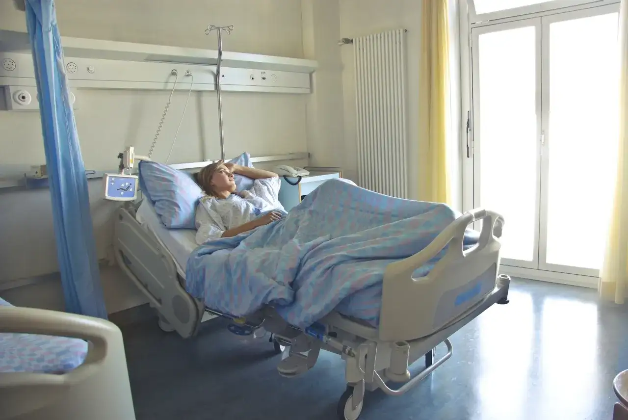 Młoda kobieta leży w szpitalnym łóżku, zastanawiając się, **l4 co to** za choroba ją dopadła.