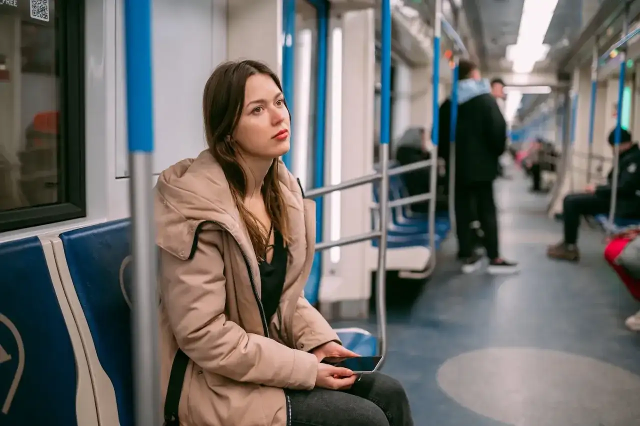 Młoda kobieta w beżowej kurtce siedzi w metrze, zamyślona. Może właśnie wraca z wizyty u lekarza, który wystawił jej zwolnienie lekarskie z powodu wypalenia zawodowego.