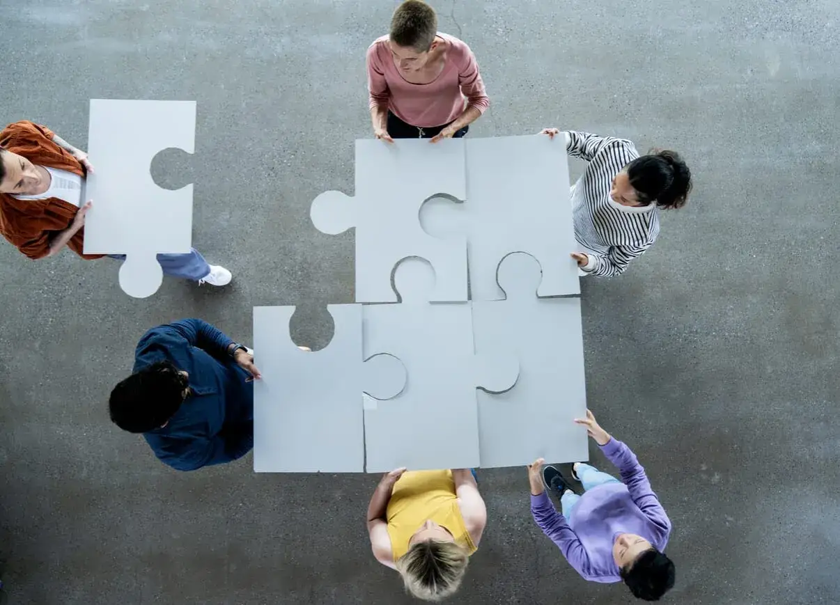 Ludzie składają puzzle, symbolizując współpracę. Czy jednoosobowa działalność gospodarcza może zatrudniać pracowników? Tak, to możliwe!