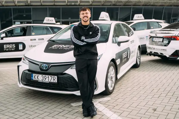 Młody kierowca Ubera z dumą pozuje przy białych autach. Zastanawiasz się, ile można zarobić w Uberze?