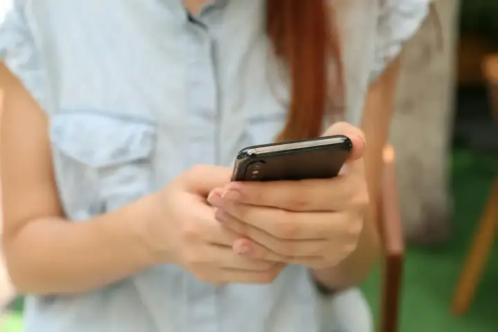 Kobieta z rudymi włosami trzyma smartfon, szukając informacji, gdzie sprawdzić L4.